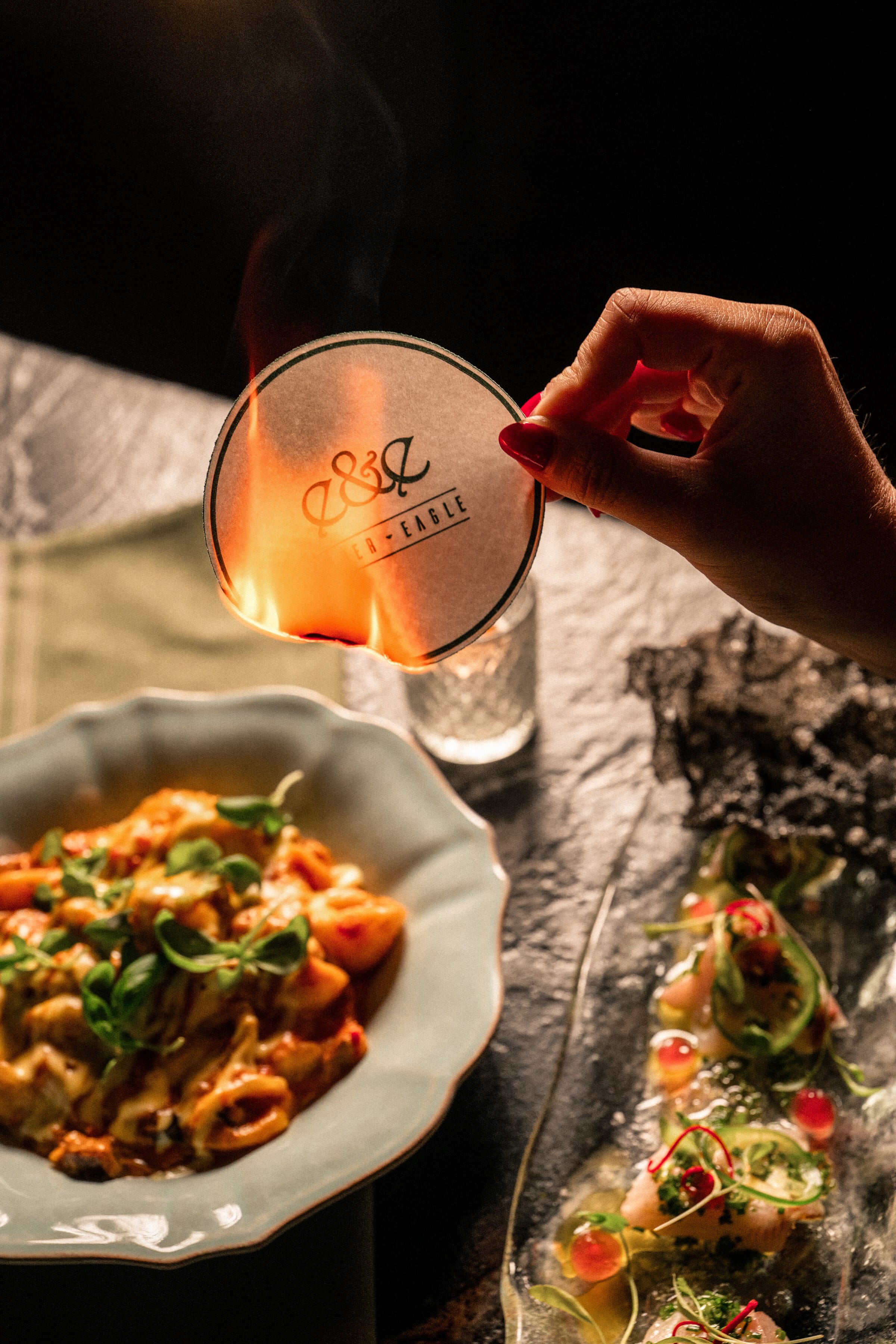 An Ember & Eagle coaster aflame above house-made pasta and crudo